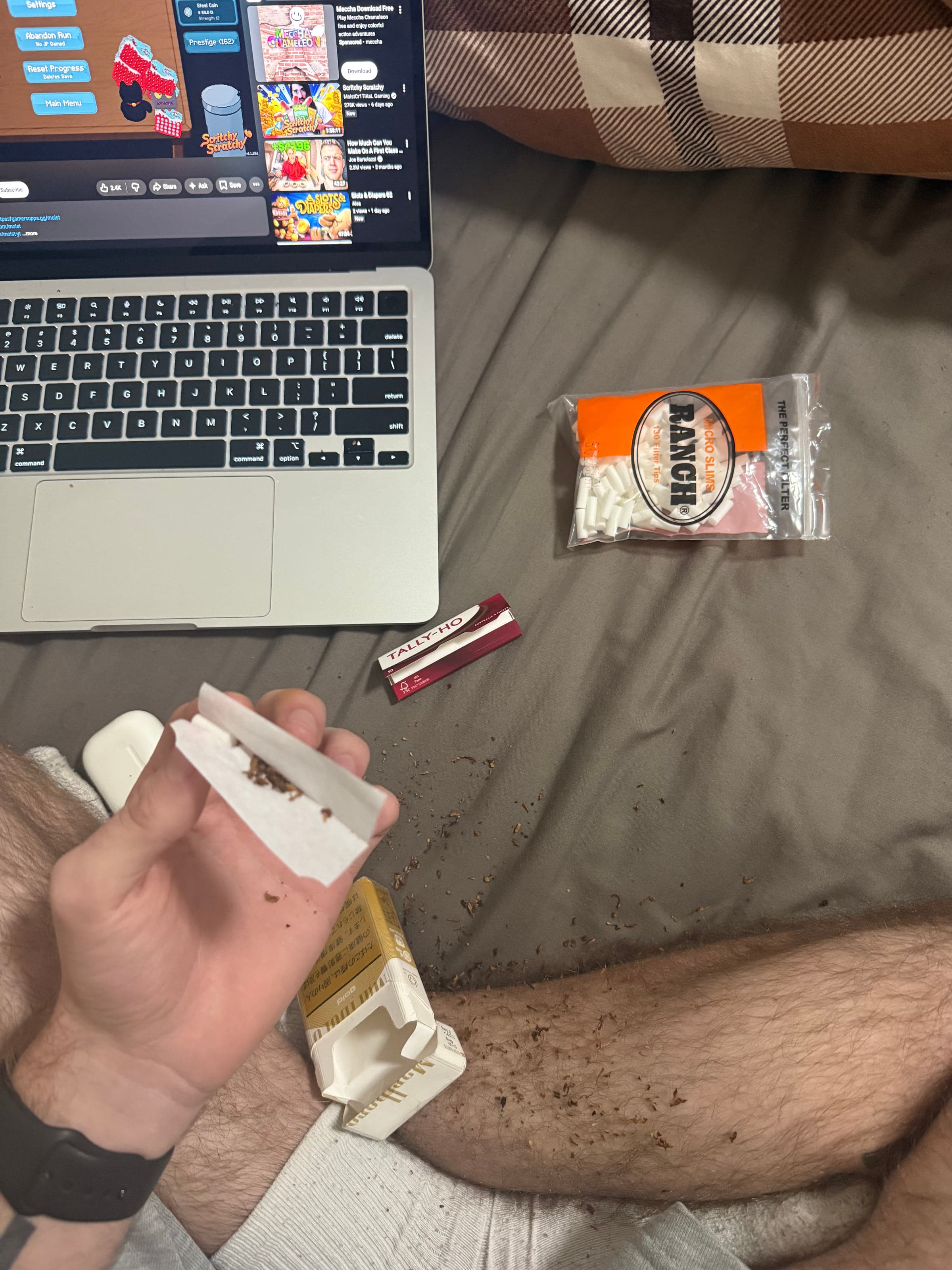 A laptop, rolling papers and tobacco on a bed